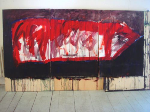 Grossformatiges dreiteiliges Bild mit roter Pfeilform auf dunklem Grund, an eine Atelierwand gelehnt