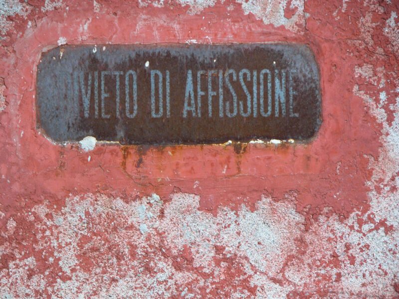 Rostige Metalltafel «Divieto di affissione» auf abblätternder roter Wand mit weissen Flecken, Fotografie aus der Serie «Alltägliche Fundstücke I»