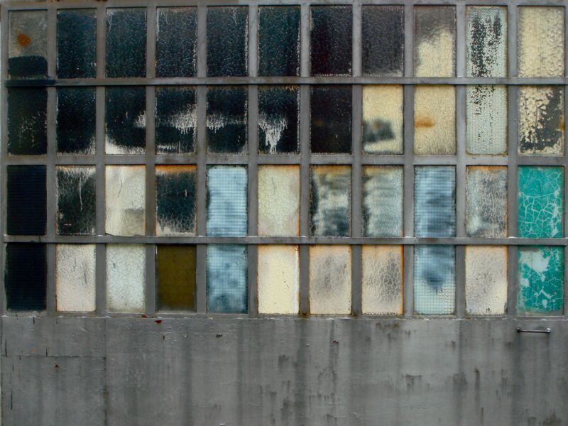 Raster aus Glasfeldern in Schwarz, Beige, Blau und Türkis über einer grauen Betonwand, Fotografie aus der Serie «Alltägliche Fundstücke II»