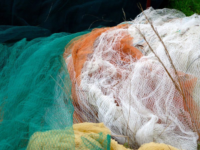 Nahaufnahme zusammengeknüllter Netze in Türkis, Orange, Weiss und Gelb mit trockenen Halmen, Fotografie aus der Serie «Agaven, Oliven, Kakteen»