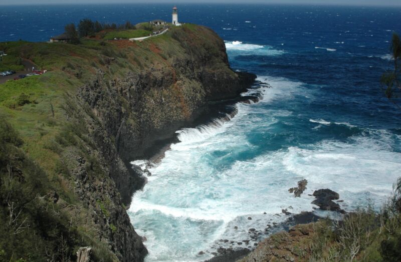 Steile grüne Klippe mit Leuchtturm auf der Spitze über tiefblauem Meer und weisser Brandung, Fotografie aus der Serie «Hawaii»