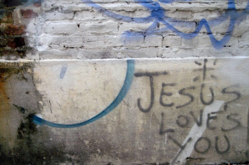 Graffiti «Jesus loves you» und ein blauer Bogen auf einer verwitterten weissen Mauer, Fotografie aus der Serie «Honolulu»