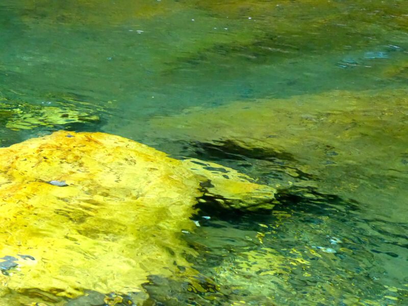 Leuchtend gelber Stein unter türkis-grünem, leicht bewegtem Wasser, Fotografie aus der Serie «An ligurischen Flüssen und Bächen»