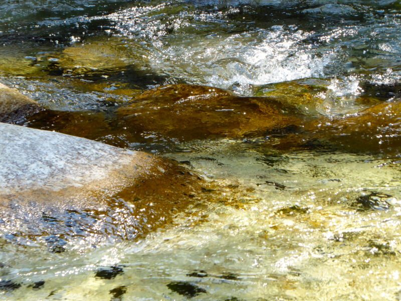 Sonnenbeschienenes, flach strömendes Wasser über hellen und braunen Felsen, Fotografie aus der Serie «An ligurischen Flüssen und Bächen»
